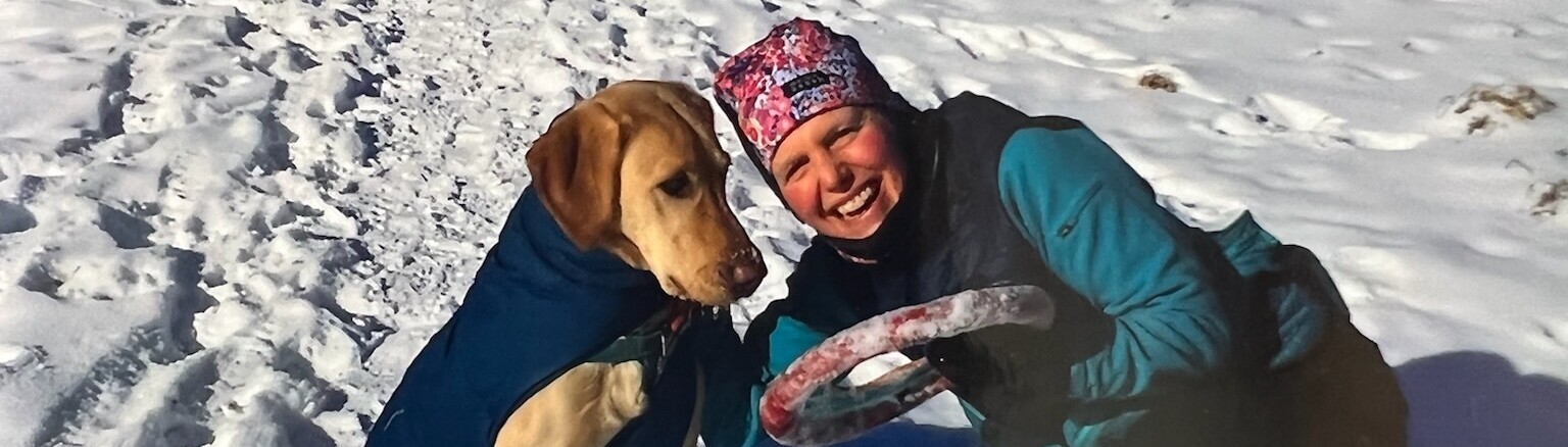 A Woman & a Labrador Retriever in the Snow Wearing Their Winter Gear